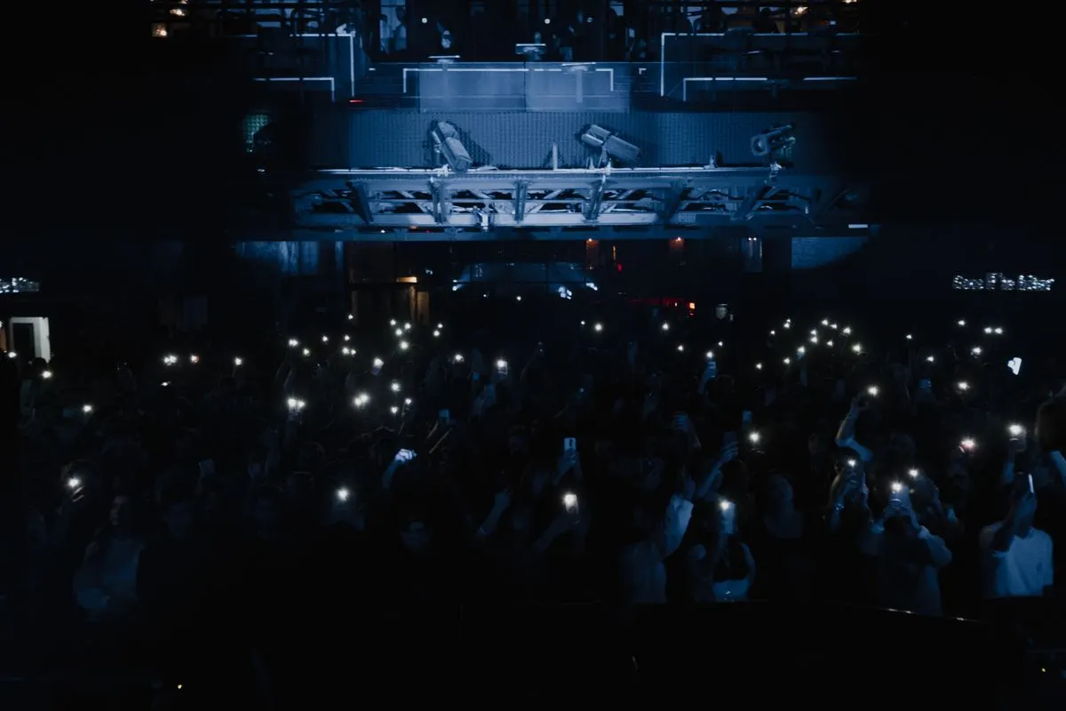 A concert crowd holding up glowing phones in the dark